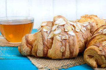 Freshly baked croissants with almond flakes,  cup of tea on a blue wooden background. French pastries. Breakfast.