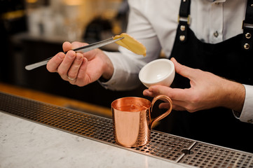 Bartender in apron making alcoholic cocktail with ginger using tongs