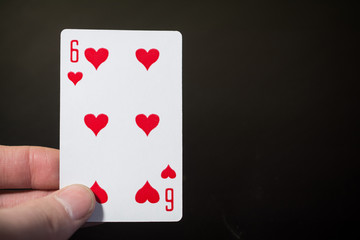 Abstract: man hand holding playing card six of hearts on a black background with copyspace