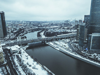 aerial drone shot of the city skyscraper near the river and bridge during winter