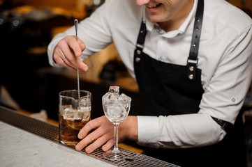 Barman mixes up ice in whiskey using spoon