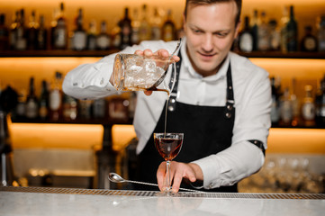 Barman at the pub pours cold whiskey in goblet
