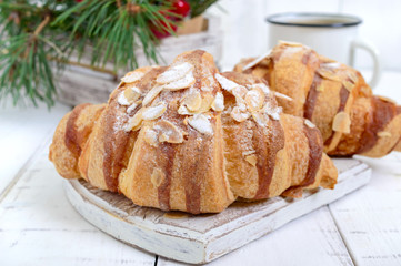 Large tasty croissants with almond flakes and a cup of tea on a white wooden background. French pastries. Breakfast.