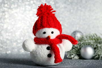 Small snowman toy with baubles and fir-tree branches on lights background