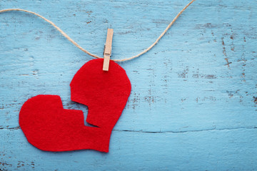 Broken red heart hanging on rope on blue wooden table