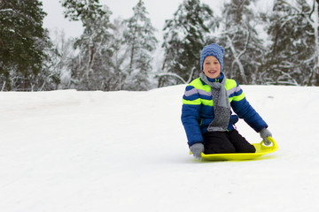 Fototapeta na wymiar Kid slides down a hill on plate for driving on snow