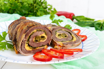 Delicious meat roll with spinach, cheese and pickled cucumber on a plate on a white wooden background.