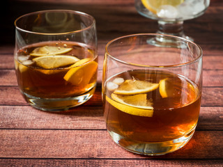 Glasses of cocktail with ice and lemon on wooden table close-up