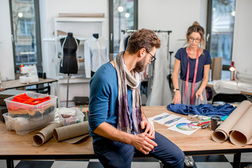 Obraz premium Couple of fashion designers working with fabric and clothing sketches at the studio full of tailoring tools and equipment