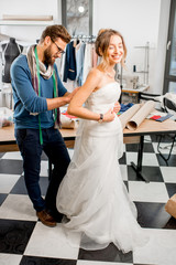 Naklejka premium Young woman client fitting wedding dress with man tailor standing at the sewing studio