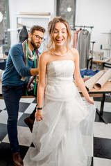 Young woman client fitting wedding dress with man tailor standing at the sewing studio