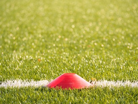 Bright red plastic cone on painted white line of soccer field. Plastic football green turf playground