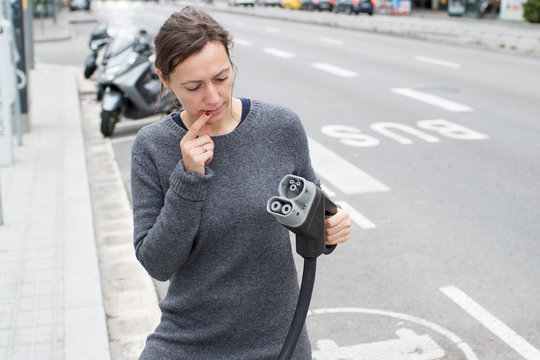 Frau verwirrt mit Stecker fuer Elektroauto an der Strasse