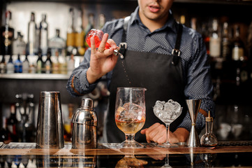 Bartender pours syrup in cocktail glass with ice