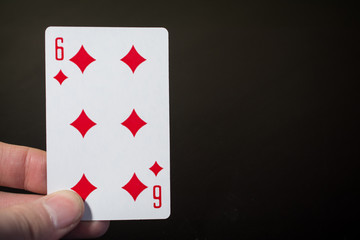 Man hand holding playing cards six of diamonds isolated on black background with copyspace abstract