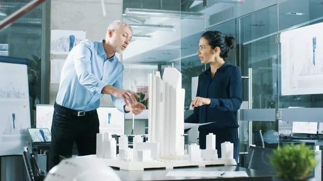 Two Professional Male and Female Architectural Engineers Work with Blueprints and on a Building Model Design for the Urban Planning Project.  Shot on RED EPIC-W 8K Helium Cinema Camera.