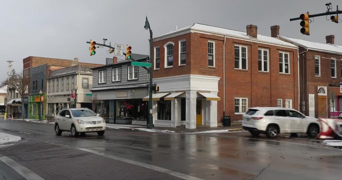 A daytime winter establishing shot of businesses on a typical Main Street in America decorated for Christmas. Building names obscured for general use. Snow plow truck passes by. Pittsburgh suburb.  	