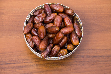 Dates fruit on a silver bowl on wooden table. The Muslim feast of the holy month of Ramadan Kareem