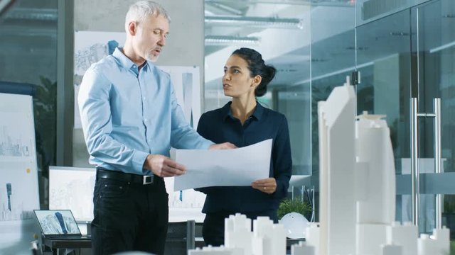 Two Professional Male and Female Architectural Engineers Work with Blueprints, Discussing Building Model Design for the Urban Planning Project. Shot on RED EPIC-W 8K Helium Cinema Camera.
