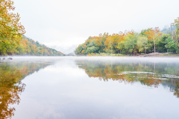 Fototapeta na wymiar New River Gorge wide canyon water river lake during autumn golden orange foliage in fall by Grandview with peaceful calm tranquil morning bright mist fog