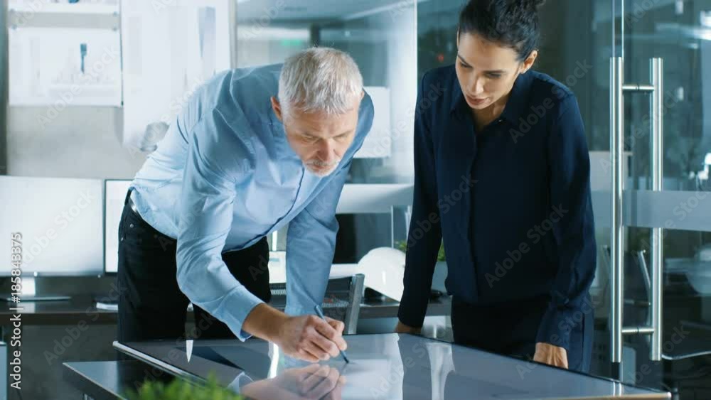 Poster senior male and young female architectural designers draw building concept on a graphics tablet disp