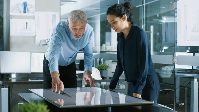 Senior Male and Young Female Architectural Designers Draw Building Concept on a Graphics Tablet Display Vertical Touchscreen Table. They Use Gestures for Zooming Project Model. 
