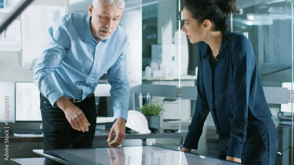 Poster senior male and young female architectural designers draw building concept on a graphicstablet displ