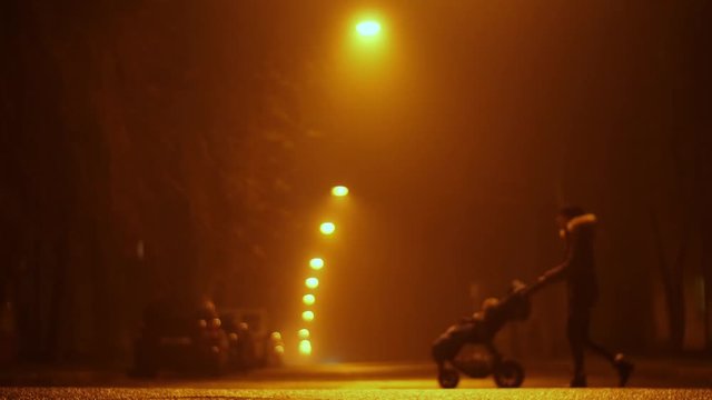 empty night street in the defocus and fog. lanterns hang over the road,a woman with a stroller crosses the road