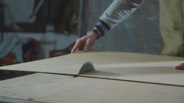 Circular table saw cutting wood sheet at carpenter workshop in slow motion