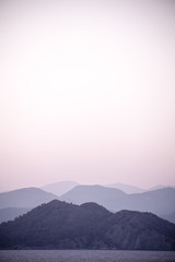 Layers of hill silhouettes, forming different shades of blue and grey, merging with the sea on a shoreline, peaceful and tranquil view