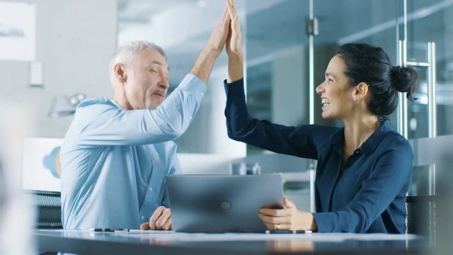 Senior Executive and Young Female Manager Working on a Laptop Win Big and Have Successful Moment, They High Five Each other and are Happy.  Shot on RED EPIC-W 8K Helium Cinema Camera.