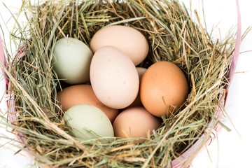Easter basket filled with farm fresh eggs and hay on a white background