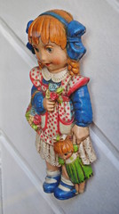 Duas bonecas uma a segurar a outra penduradas numa parede branca em madeira