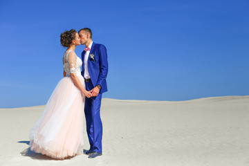 Fototapeta na wymiar Young wedding couple on beautiful sand dune with wives on sea 