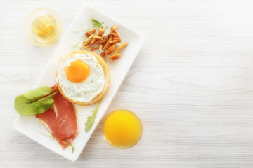 Breakfast with fried egg on bread, bacon, mushrooms, greens. Sauce and fresh juice. View from above