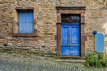 Fototapeta na wymiar Pale blue and worn door and windows on the stone walls of a sma
