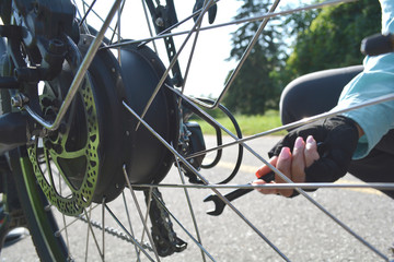 Fitness sport cyclist female is repairing electric bicycle with the key tool in the park. Young...