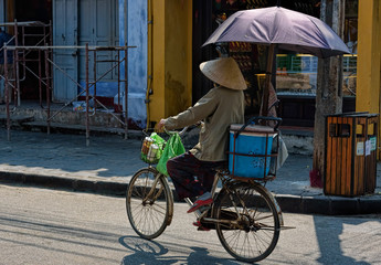 Fototapeta na wymiar Woman riding a bike with umbrella in the streets of Hoi An, Viet