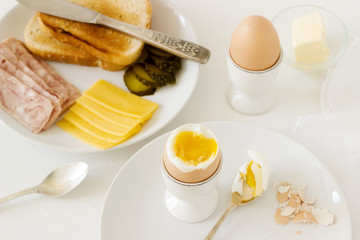 Breakfast with soft-boiled egg, bread toast, ham, cheese and canned cucumbers. Rustic style.