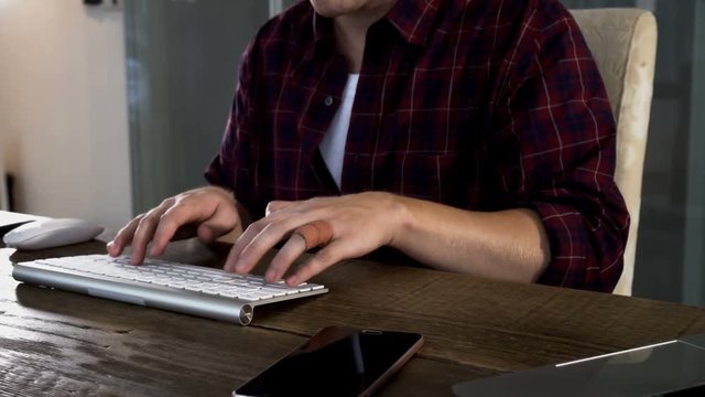 The handsome caucasian is typing on wireless keyboard on wooden table
