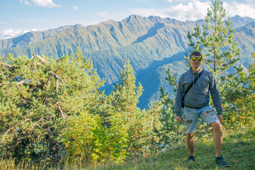 Naklejka premium Turysta w krótkich spodenkach i bluzie stoi na klifie na tle drzew i ogląda przepiękne widoki. Piękne chwile cud natury. Mestia