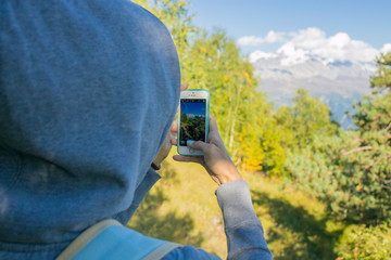 So beautiful woman standing on top of a mountain in the hood with a backpack. Back. looking at the mountains and trees from the top.Beautiful view. Photographs on the phone Mestia