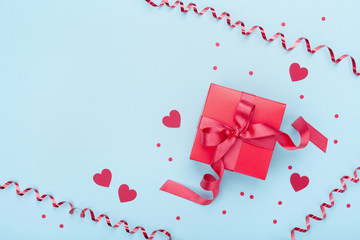 Red gift box, serpentine, hearts and confetti on blue background top view. Valentine's day greeting card. Flat lay.