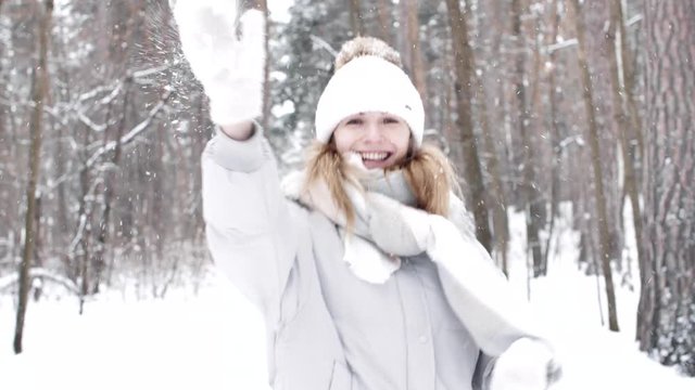 Cheery active woman is throwing snowball in wintertime.