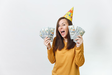 Beautiful caucasian lucky young happy woman in yellow clothes, birthday party hat holding wad of cash money, celebrating holiday on white background isolated for advertisement. Winner with dollars.