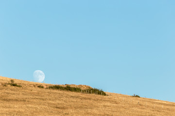 Moon rising up behind an hill, in an empty, blue sky