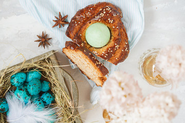 Traditional Greek Easter bread - tsoureki, sliced in Easter decorations with painted blue quail eggs in the nest and flowers. Top view.