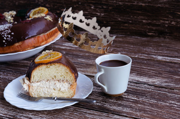 Roscon de reyes slice and cup of hot chocolate on wooden background. Traditional Spanish Christmas cake with crown to cerebrate Epiphany or Dia de Reyes Magos , Three Wise Men Day.