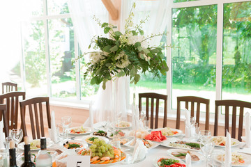 Beautiful wedding floral decoration on a table with catering food in a light restaurant hall with white tablecloths