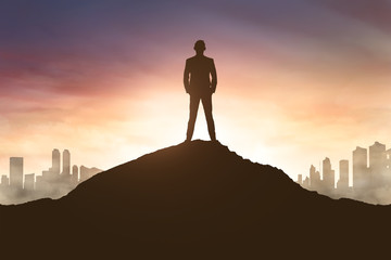 Silhouette of businessman on mountain top with cityscape view